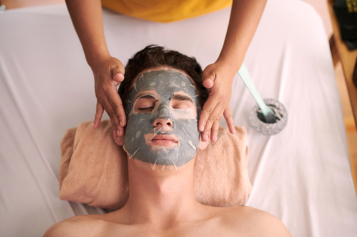 Cosmetologist covering face of client with sheet mask