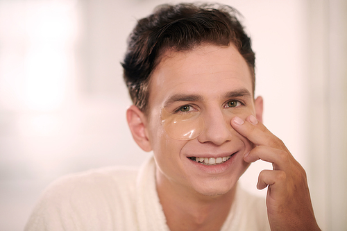 Portrait of happy young man applying patches to eliminate dark circles, wrinkles and puffiness