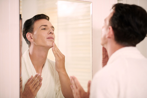 Young man applying moisturizing face lotion after morning shower