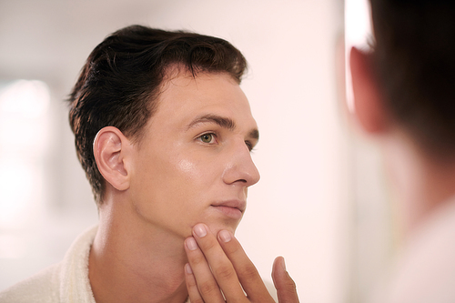 Portrait of young man applying brightening face lotion after evening shower