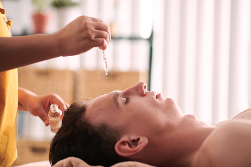 Beautician applying rejuvenating serum on face of young man