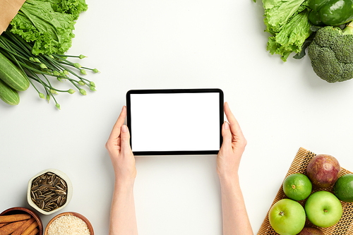 Hands of woman holding tablet computer with empty screen on table with groceries