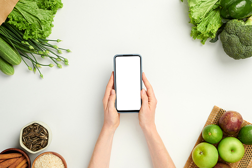 Hands of person holding smartphone with empty screen when ordering fresh fruits and vegetables online