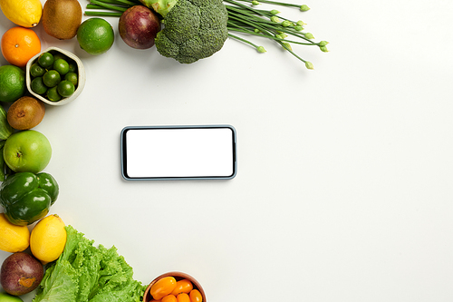 Smartphone with empty screen on white table next to organic fruits and vegetables