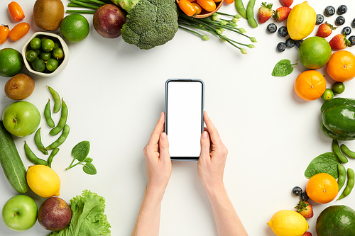 Hands of person holding smartphone with empty screen over table with groceries