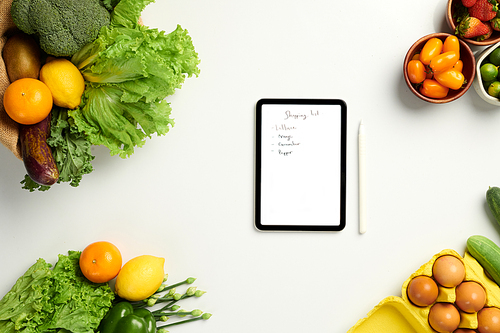 Tablet computer with handwritten shopping list on table with groceries