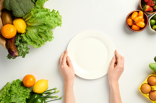 Hands of person putting empty plate on table with fresh fruits and groceries, view from the top