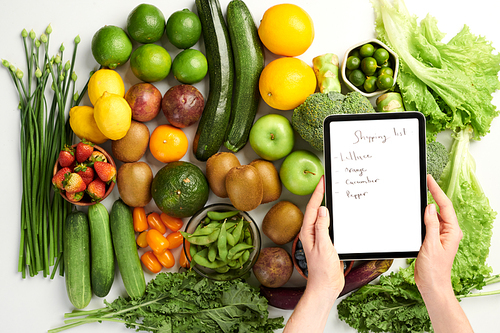 Hands of person holding tablet computer with shopping list over table with groceries