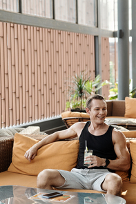 Joyful fit man resting on sofa in lounge area of fitness center