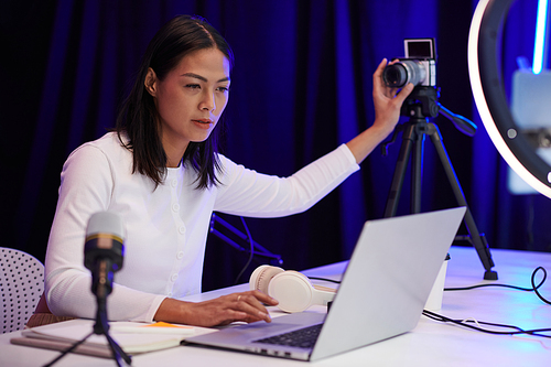 Blogger setting camera and checking picture on laptop before filming video for her channel