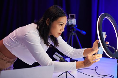 Blogger attaching smartphone in front of ring light to get better quality footage