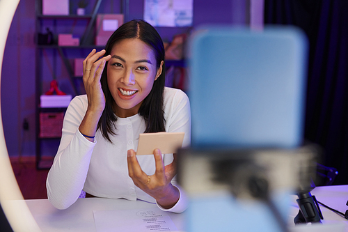 Smiling blogger filming herself doing makeup