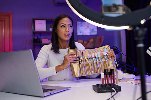 Beauty blogger filming review of makeup brushes set in golden case