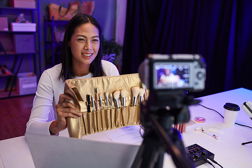 Smiling beauty blogger filming review of new set of brushes