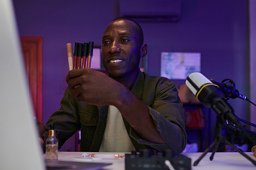 Cheerful Black man filming review of liquid lipsticks from seasonal collection