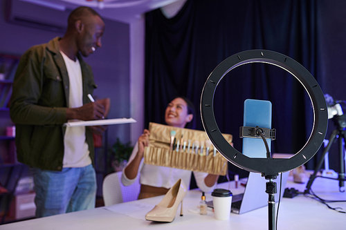 Ring light with attached smartphone on table in filming studio of fashion blogger