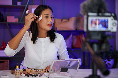 Smiling woman filming herself doing face massage with quartz roller