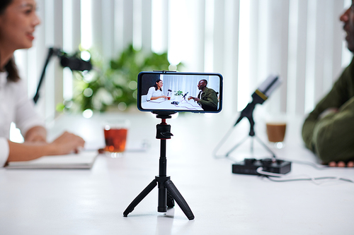 Smartphone recording podcaster talking to guest at big table