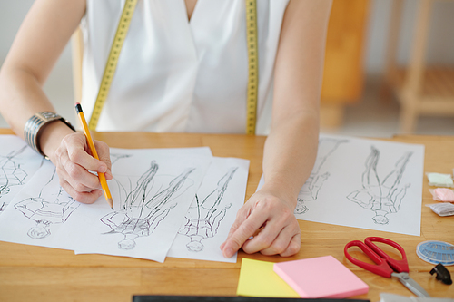 Tailor sitting at desk in her studio and drawing sketches for clients