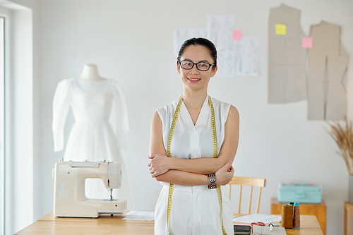 Smiling seamstress standing in front of desk with sewing machine