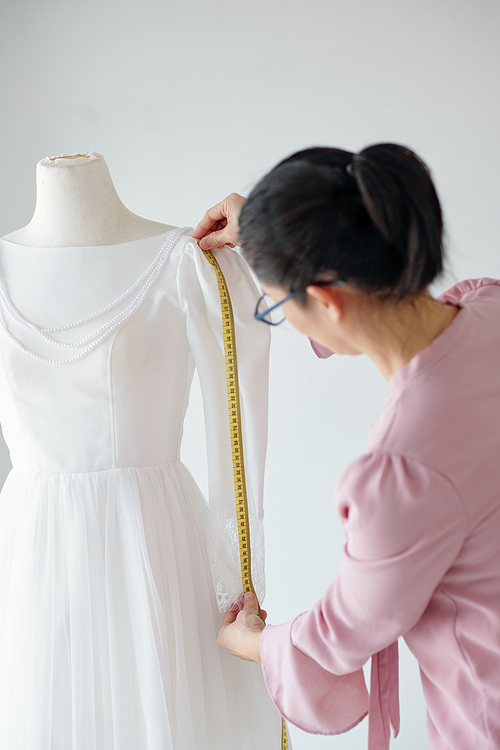 Tailor measuring sleeve of wedding dress she is making for client