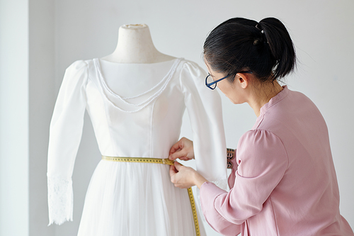 Tailor measuring waist of mannequin when working on dress for client