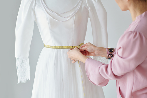 Seamstress measuring waist of mannequin with wedding dress