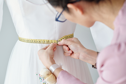 Seamstress double checking waist length of dress on mannequin