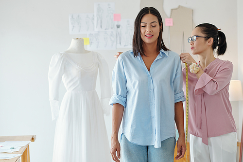 Tailor measuring shoulders of customer who ordered dress for wedding