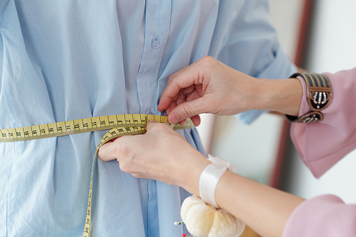 Hands of seamstress measuring waist of female client