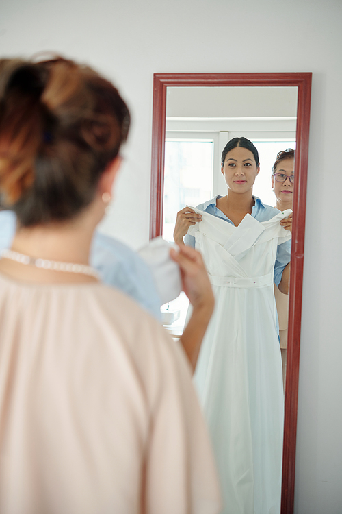 Smiling bride trying on wedding dress in front of mirror in wedding salon