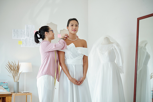 Smiling bridal salon assistant helping client to wear pearl necklace