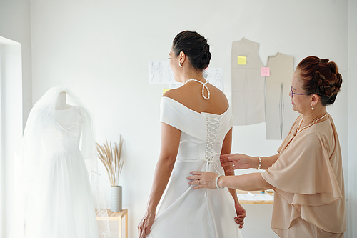 Mother helping daughter to tighten corset on wedding dress