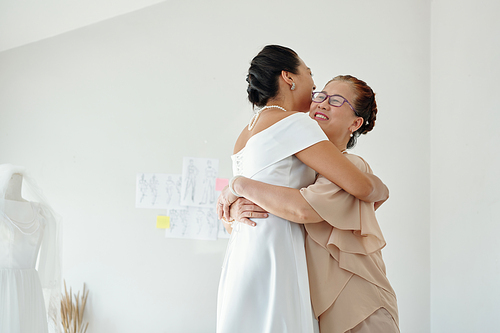 Happy senior woman hugging her daughter in wedding dress