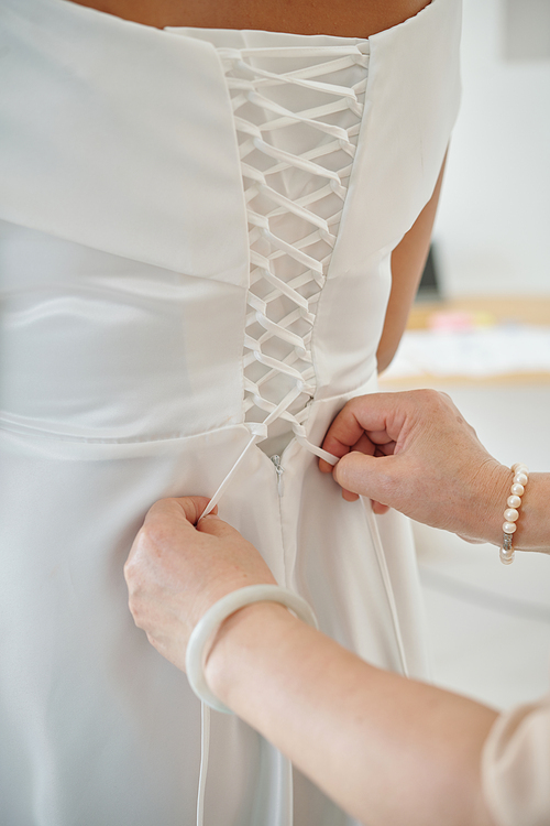 Mother helping daughter to tie up corset of wedding dress