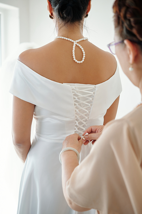 Elegant bride asking mother to tighten corset on wedding dress