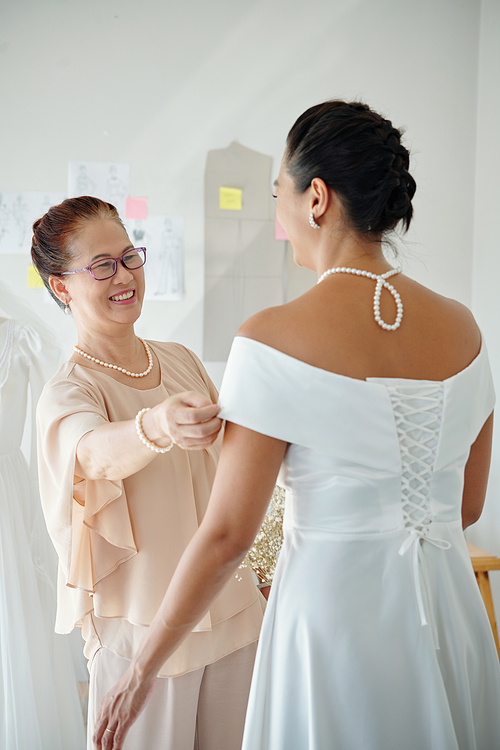 Happy proud mother looking at her adult daughter in beautiful elegant wedding dress