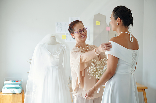 Happy mother looking at daughter wearing elegant white wedding dress