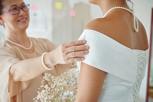 Smiling mother supporting her daughter standing in wedding dress in atelier