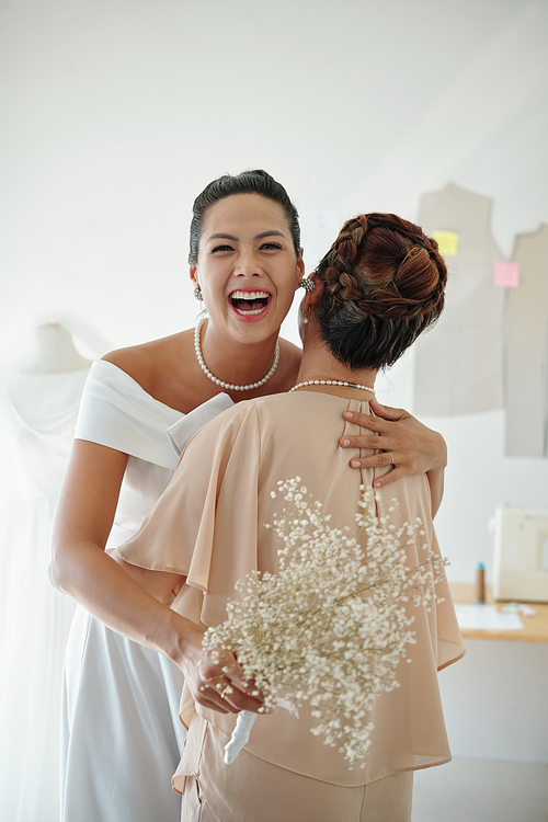 Happy excited bride with bouquet in hands hugging her mother