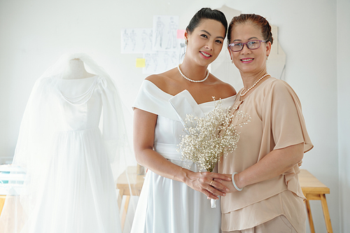 Happy bride with her mother on wedding day holding flowers and smiling at camera