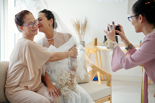 Bride kissing her mother of cheek when tailor photographing them for social media