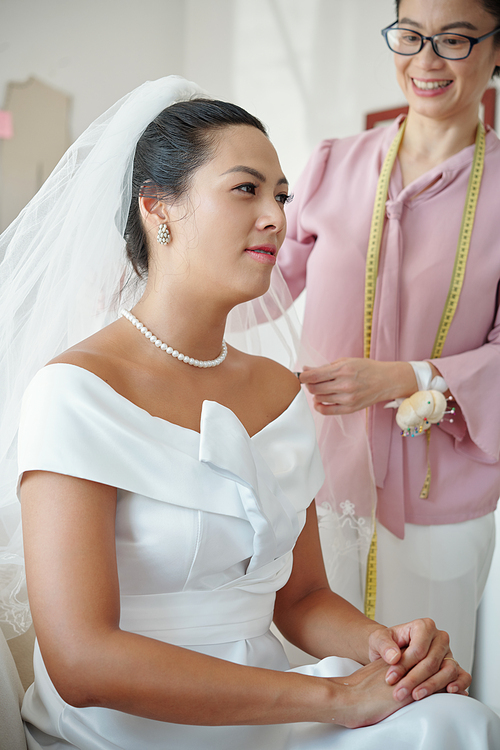 Happy tailor looking at elegant bride wearing wedding dress she created