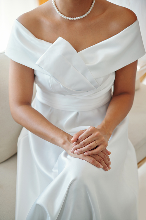 Cropped image of bride wearing white elegant wedding dress and pearl necklace