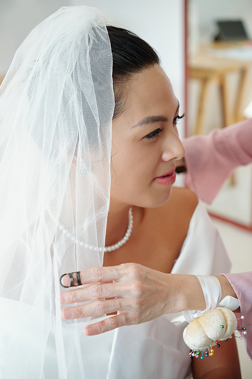 Tailor helping bride to wear veil for wedding ceremony