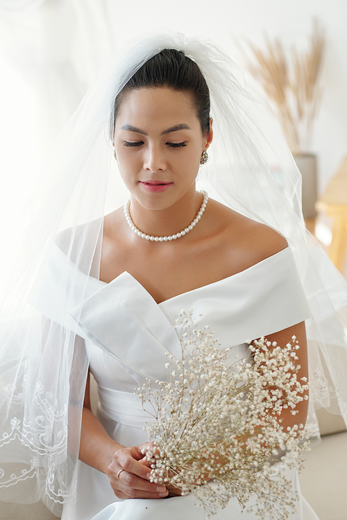 Beautiful bride in elegant dress and veil holding bouquet of flowers