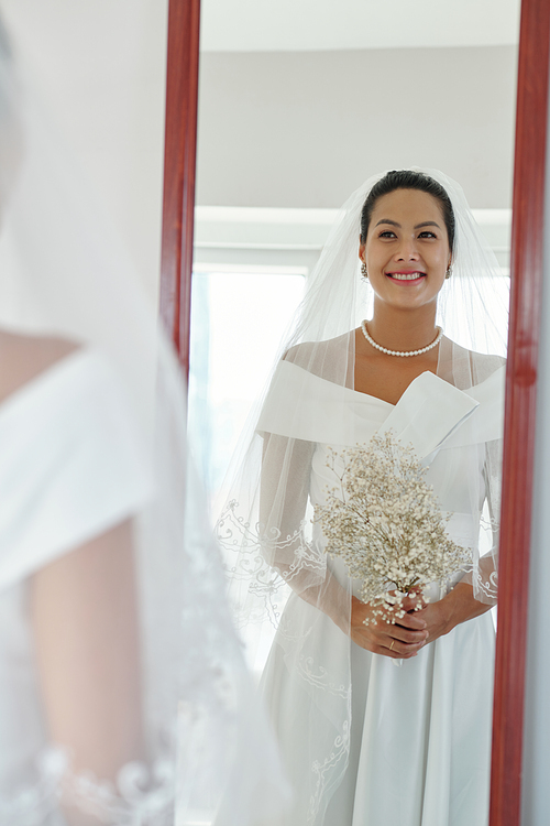 Happy bride in wedding gown looking at mirror in sewing atelier