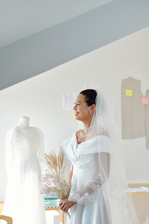 Smiling bride trying on wedding dresses and veils in sewing atelier