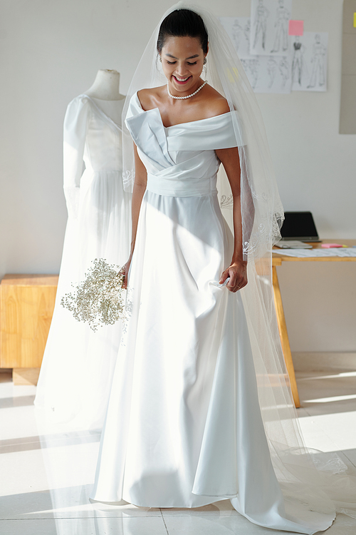 Smiling bride trying on wedding dress in fashion atelier