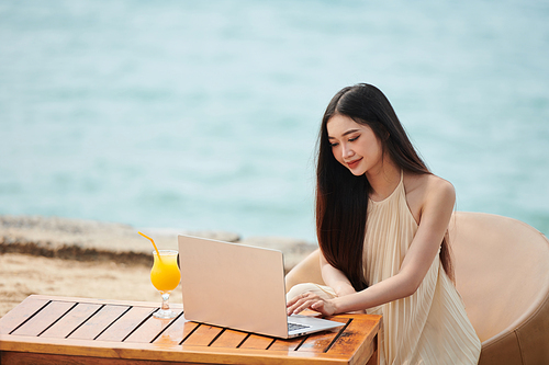 Portrait of positive young woman working on laptop on tropical beach